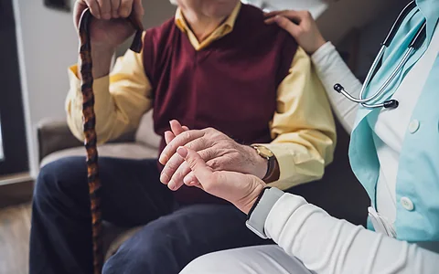 Ärztin hält die Hand eines älteren Patienten mit Gehstock